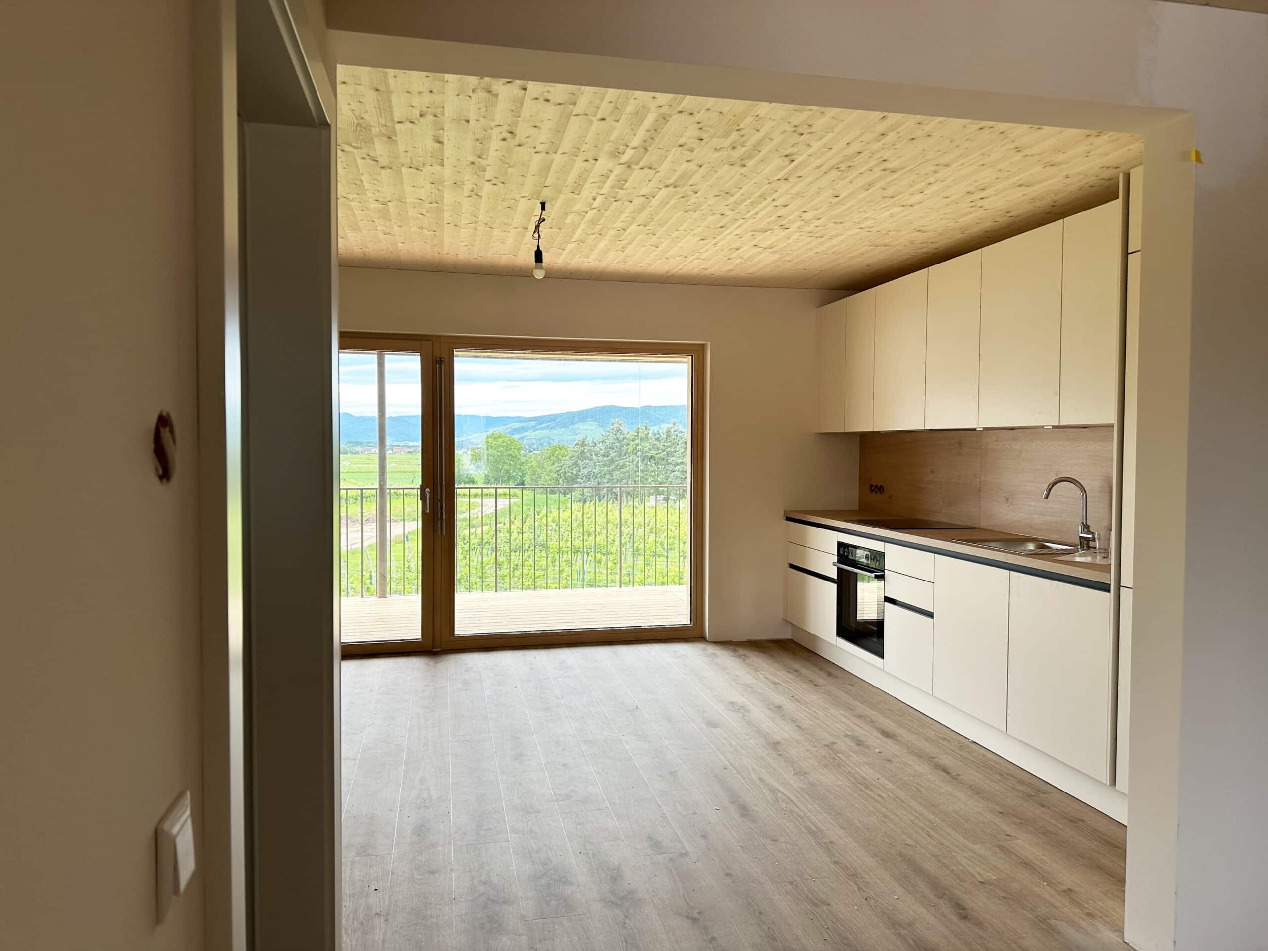 Einbauküche mit weißen Fronten und Holzrückwand in einer Wohnung in einem Massivholzbau. Architektur