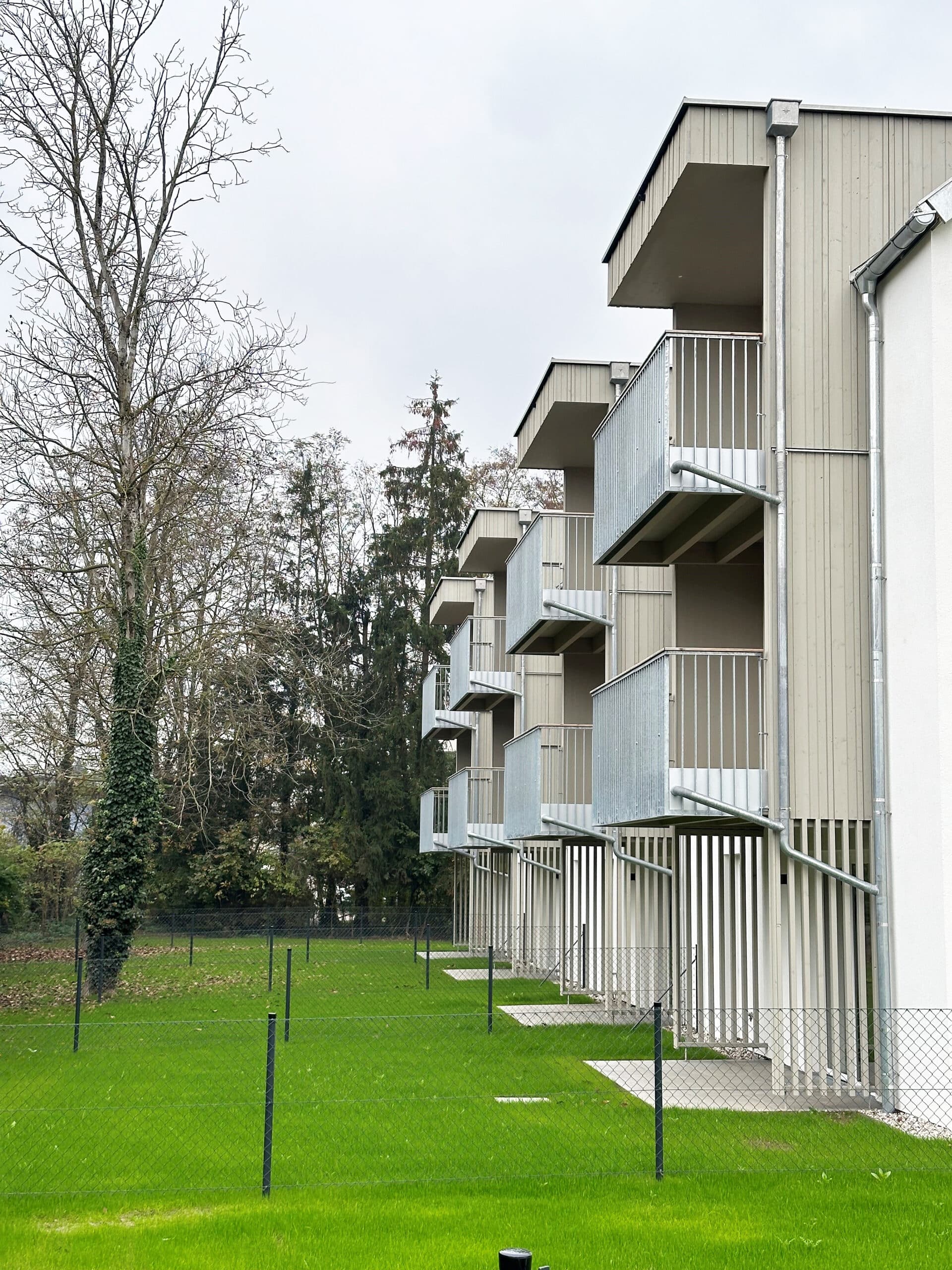 Wohnbau in Massivholz; Balkone mit Metallgeländer, Holz vorvergraut