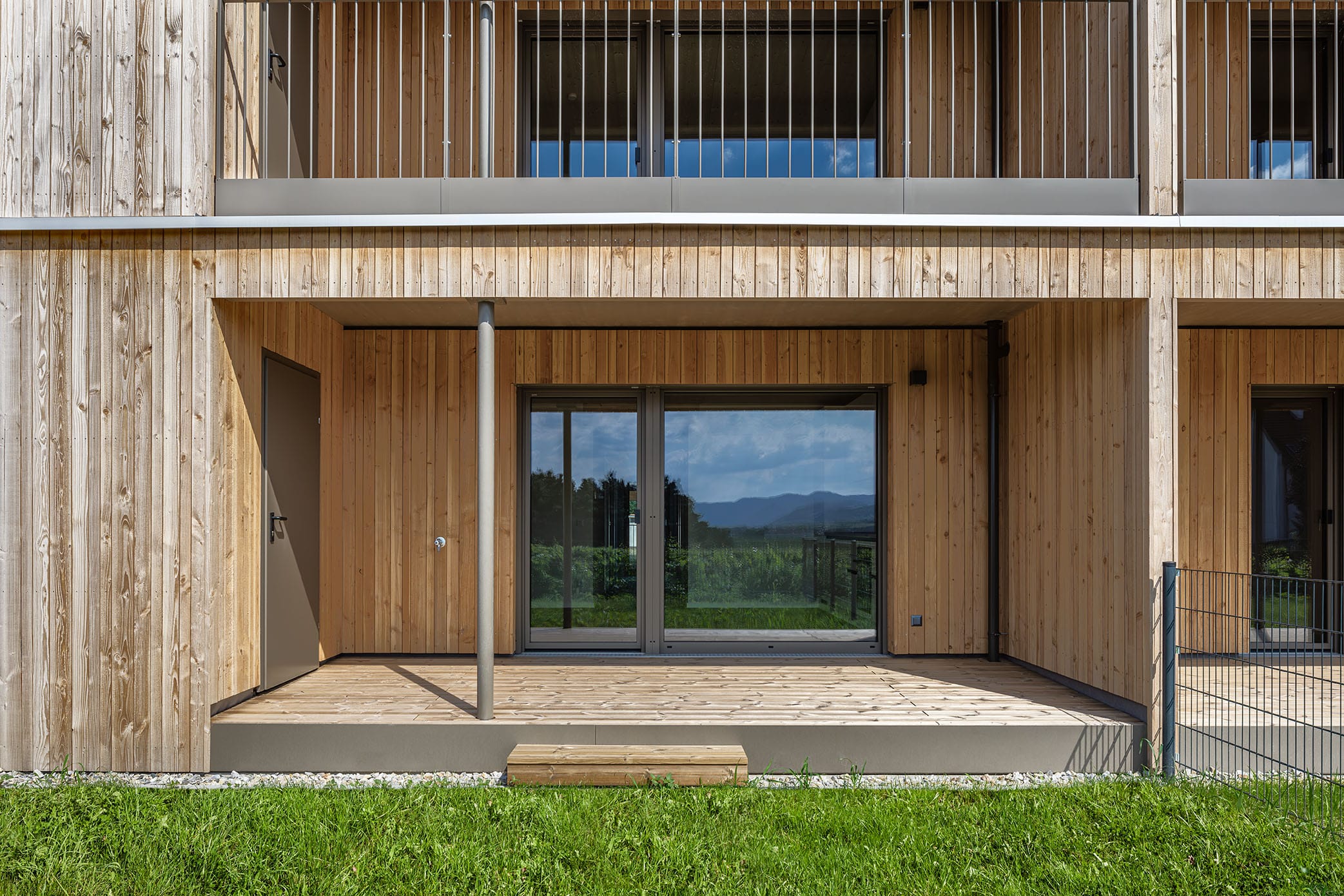 Terrasse bei Massivholzhaus mit Holzfassade und Abstellraum. Gartenansicht mit Zaun